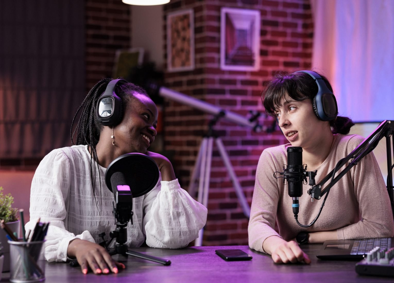 Diverse team of women enjoying podcast conversation in studio, filming online vlog and chatting for social media content. Female bloggers recording show episode at livestream station.