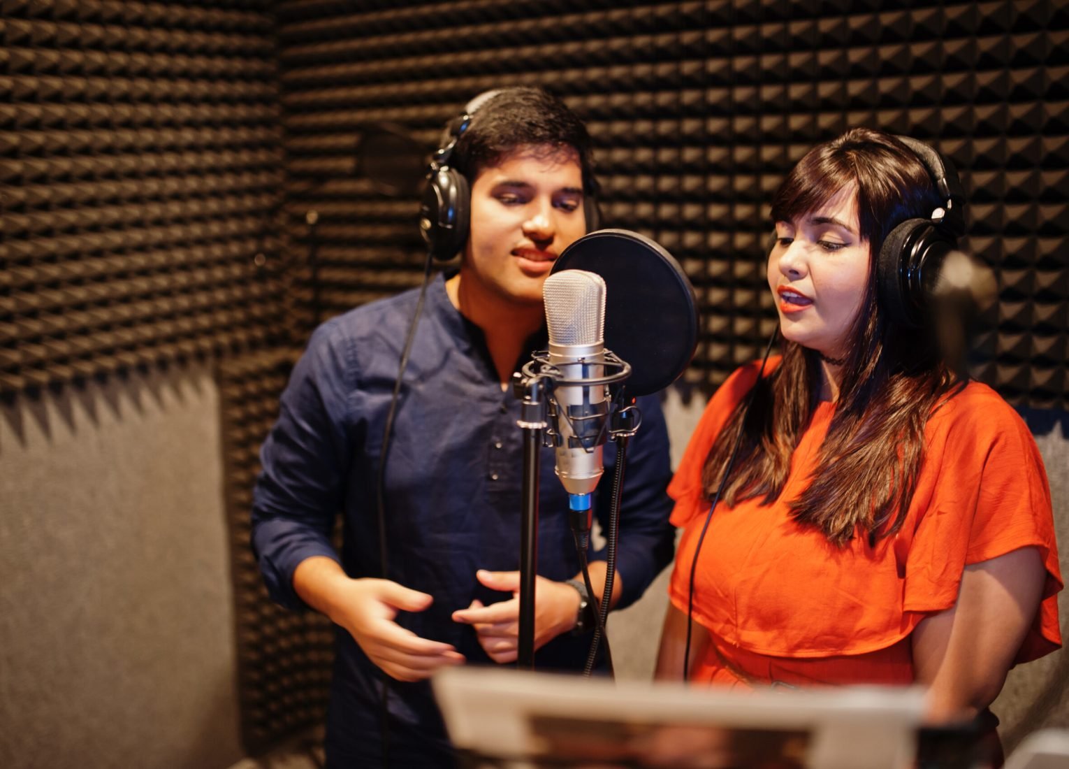 Young asian duet singers with microphone recording song in record music studio.